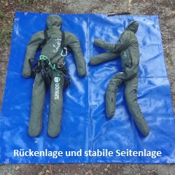 Zwei lebensgroße Puppen liegen in Rückenlage und stabiler Seitenlage auf einer blauen Plane